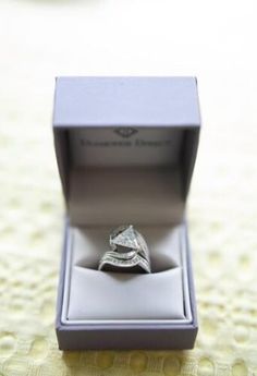 an engagement ring sits in a box on a tableclothed surface with the lid open