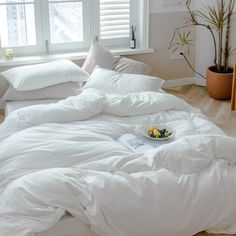 an unmade bed with white sheets and pillows on the floor next to a potted plant