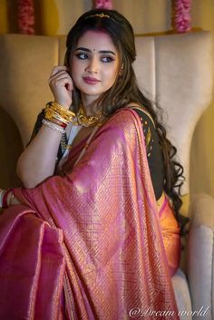 a woman in a pink sari sitting on a chair with her hand under her chin