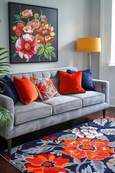 a gray couch with orange and blue pillows in front of a painting on the wall