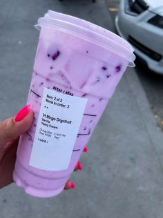 a person holding up a pink drink in front of a white car