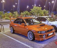 an orange car parked in a parking lot next to another white car and some lights