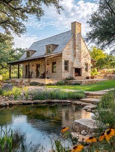 a stone house with a pond in the front yard and landscaping around it is surrounded by greenery