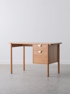 a wooden desk with two drawers on the top and one drawer at the bottom, in front of a white wall