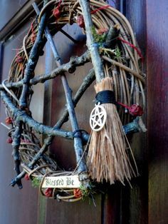 a wreath made out of branches with a wicker broom hanging from it's side