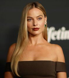 a woman with long blonde hair wearing a brown dress and green earrings at an event