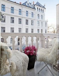 two white chairs sitting on top of a balcony next to a potted pink flower