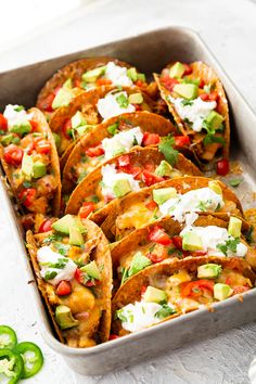 a pan filled with tacos and toppings on top of a white table next to sliced jalapenos