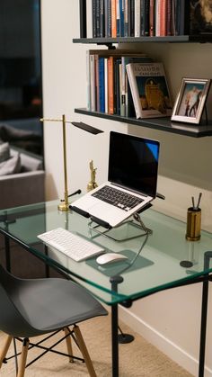 a glass desk with a laptop on it and bookshelves above the table in front of it