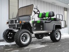 a green and black golf cart parked in front of a building with snow on the ground