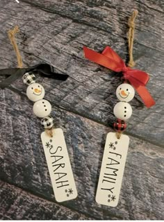 two snowmen are hanging from the side of a wooden table with red ribbon on it