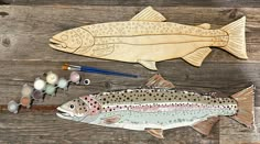 two fish are sitting next to each other on a wooden surface with paintbrushes