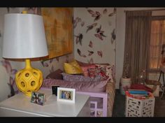 a white table topped with a yellow lamp next to a bed and dresser covered in pictures