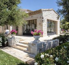 a stone house with pink flowers in the front and stairs leading up to it's entrance