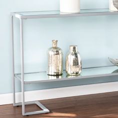 two silver vases sitting on top of a glass shelf next to a white bowl