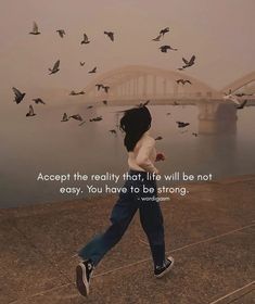 a girl running with birds flying in the air above her and a bridge in the background