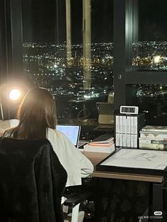 a woman sitting at a desk in front of a window with a laptop computer on it