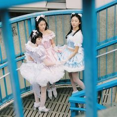 three young women dressed in costume posing for a photo on a blue metal bridge over looking the water