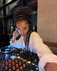 a woman in white shirt sitting at a dj's desk with headphones on