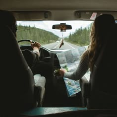 two people sitting in the back seat of a car looking at a map and drinking wine