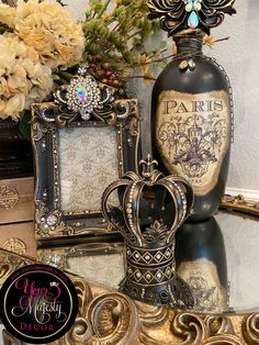 an ornate table topped with two framed pictures and a crown shaped vase filled with flowers