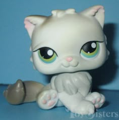 a little white kitten with green eyes sitting on a blue surface next to a toy mouse