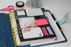 an open planner book sitting on top of a table next to scissors and markers, pens and paper