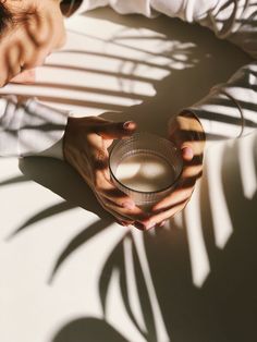 a person holding a glass in their hands on a table with shadows from the sun