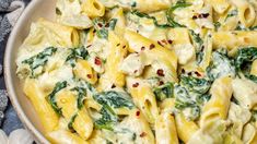 a bowl filled with pasta and spinach on top of a blue cloth next to shells