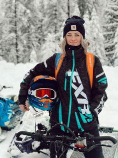 a woman standing next to a snowmobile in the snow