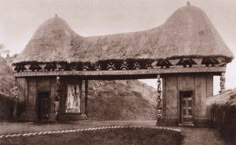 an old black and white photo of a thatch roofed building with two doorways