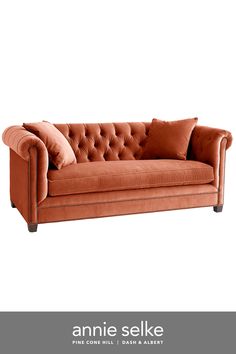 an orange couch with two pillows on it and the words annie selke above it