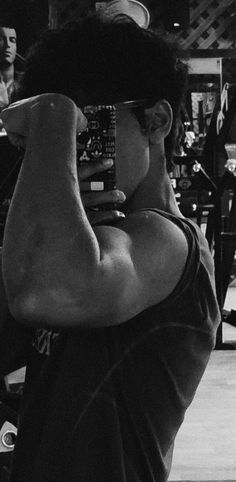 black and white photograph of man on cell phone in front of gym equipment with other people