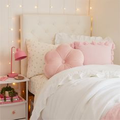 a white bed topped with pink pillows next to a night stand