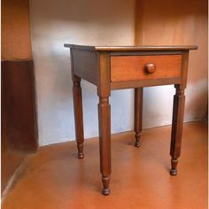 a small wooden table sitting on top of a brown floor next to a white wall