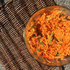 a bowl filled with shredded carrots sitting on top of a wicker tablecloth