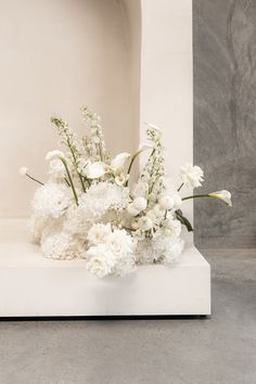 white flowers are arranged in a vase on a marble block, against a gray background