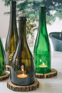 three green glass bottles sitting on top of a wooden stand with a candle in the middle