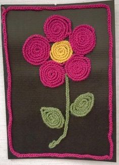 a crocheted flower on a black background with pink, yellow and green flowers