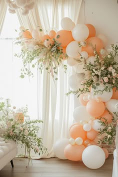 an arrangement of balloons and greenery in front of a window