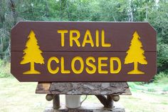 a wooden sign that says trail closed with trees on the top and yellow lettering above it