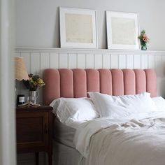 a bed with white sheets and pink headboard in a bedroom next to two pictures on the wall