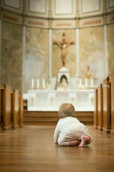 a small child sitting on the floor in front of a church alter with a crucifix behind it