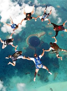 six people are floating in the air above the ocean and clouds, with their arms around each other