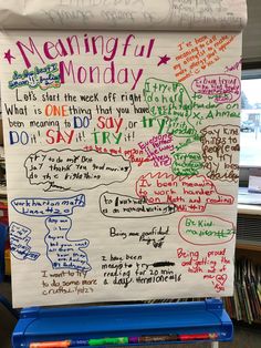 a sign with writing on it in front of a classroom desk and bookshelves