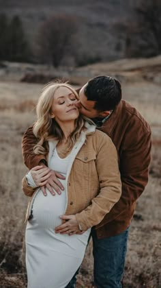 a pregnant couple kissing while standing in a field