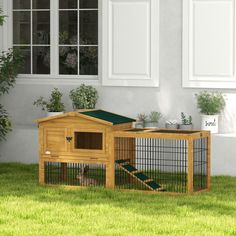 a small wooden house with a green roof in the grass next to some plants and potted plants