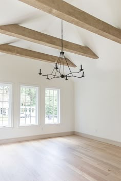 an empty room with three windows and a chandelier hanging from the rafters