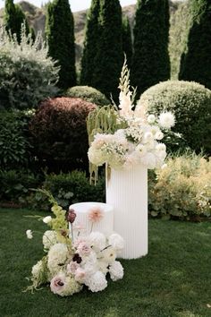 a tall white vase filled with flowers sitting on top of a lush green field