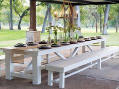 an outdoor dining table and bench set up with flowers in vases on the table